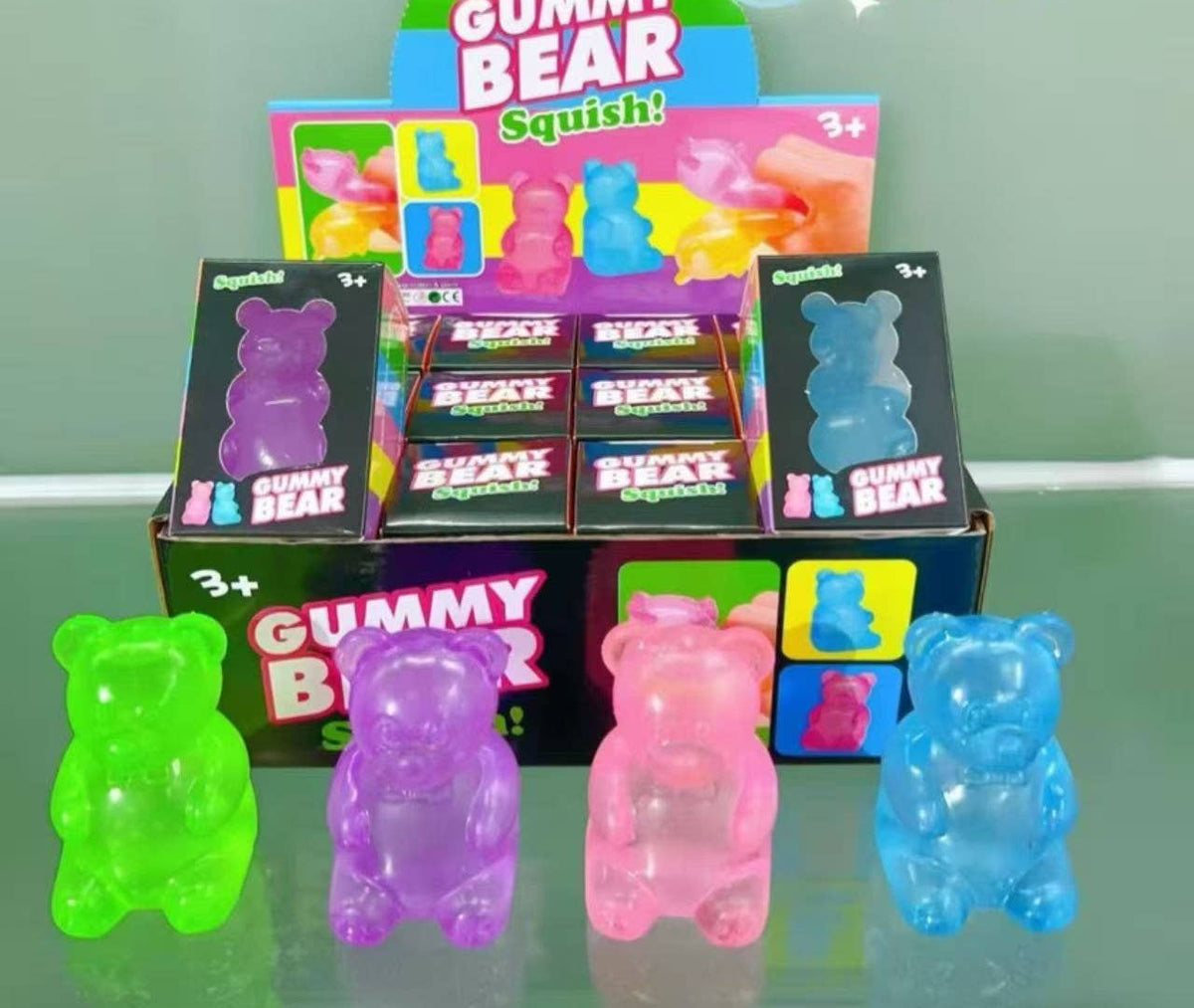 Gummy bear-shaped products with colorful packaging on a reflective surface.